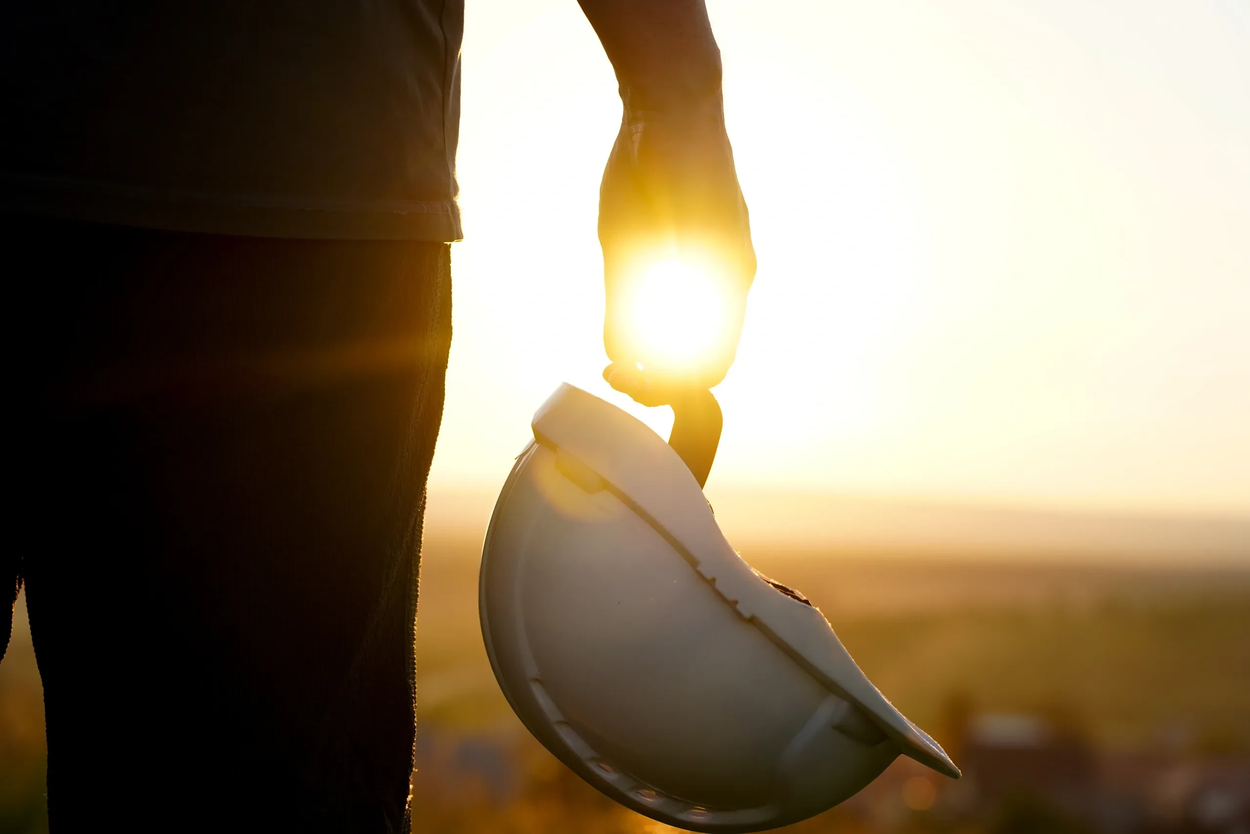 Construction professional holding hard hat at sunset